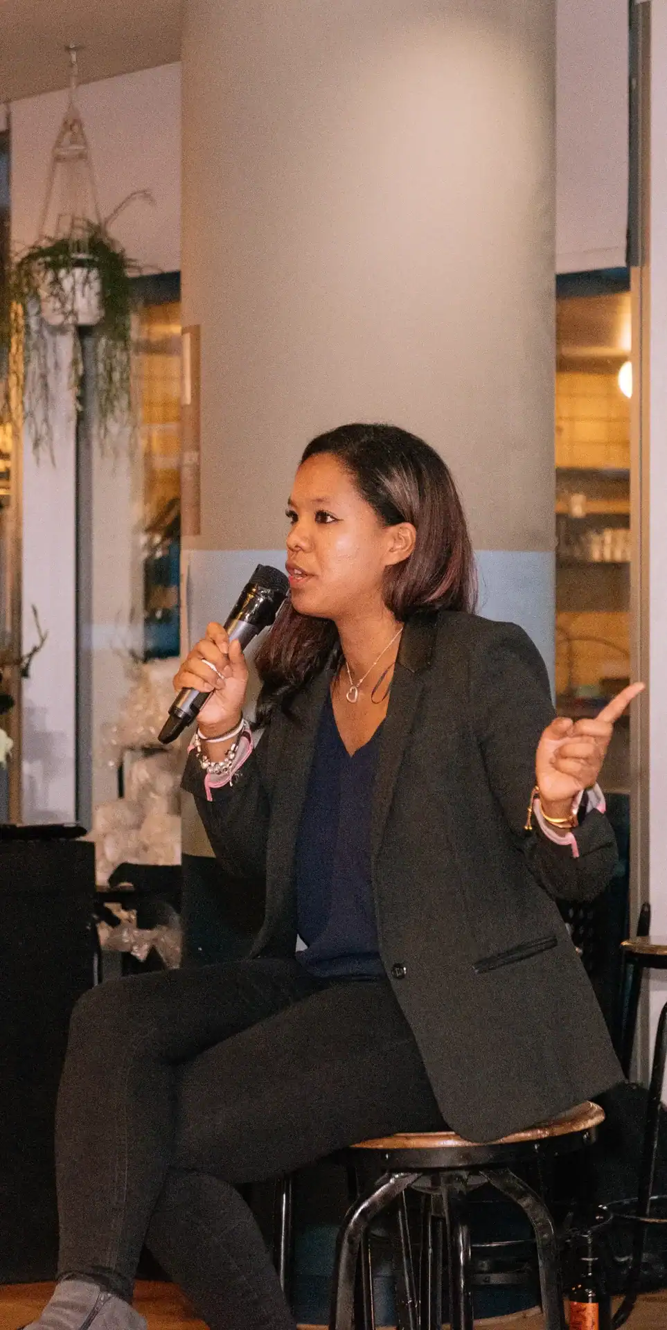 Sabrina Chevannes speaking into a microphone during a podcast interview, dressed in professional attire at an indoor event.